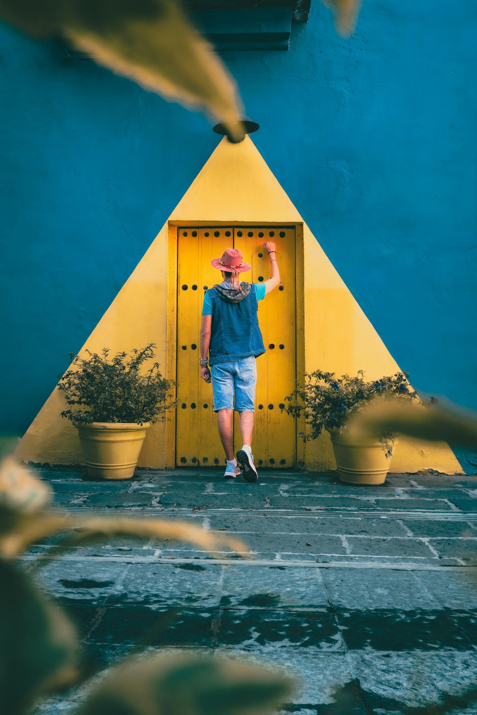 A person in a pink hat stands by a vibrant door in Puebla's colorful architecture.